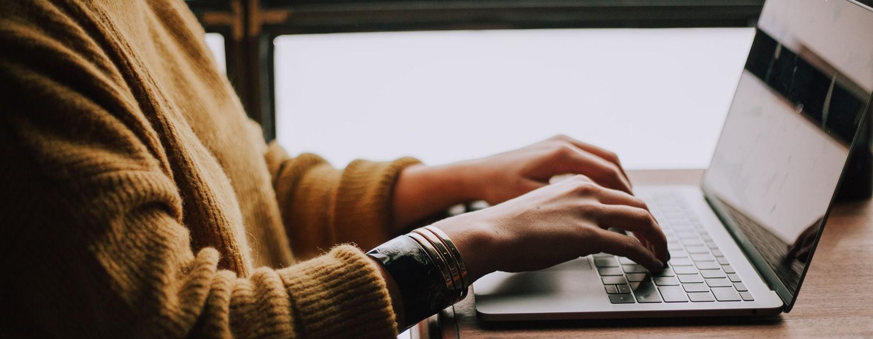 woman types on her laptop near large window